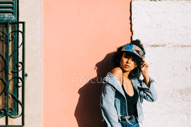 Mujer de moda en jeans y camiseta de pie y apoyado en la pared en el día soleado - foto de stock