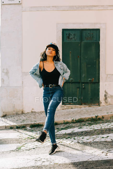 Jeune femme afro-américaine joyeuse en jeans et débardeur noir dans la rue de la ville le jour — Photo de stock