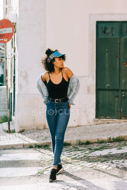 Молодая афроамериканка в джинсах и черной майке стоит на городской улице днем — стоковое фото
