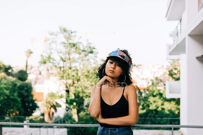 Jovem afro-americano mulher em jeans, top tanque e headband inclinado sobre trilhos e olhando para a câmera — Fotografia de Stock