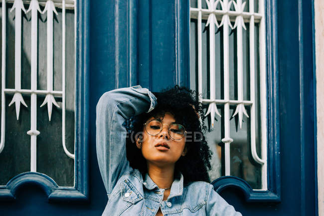 African American woman in jeans leaning on blue door and looking at camera. - foto de stock