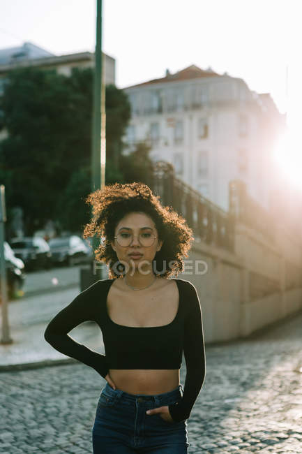 Fashionable African American woman in black top standing on sidewalk and looking at camera — Stock Photo