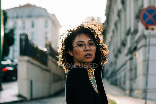 Fashionable African American woman in black top standing on sidewalk and looking at camera — Stock Photo