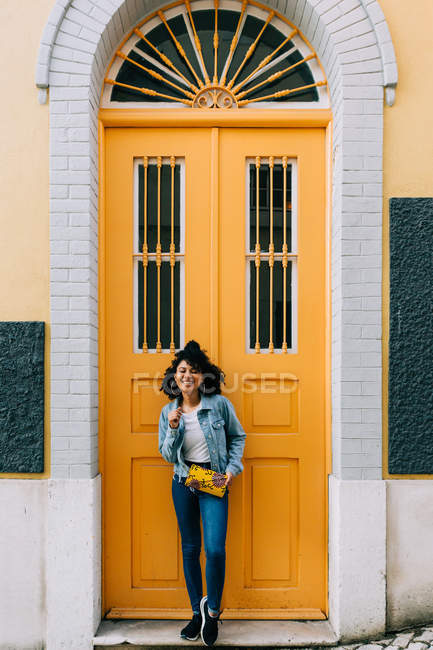 Молодая афроамериканка в джинсах и джинсовой куртке опирается на желтую дверь — стоковое фото