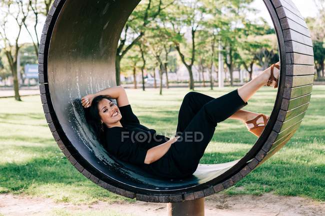 Vue latérale de la femme allongée sur un banc créatif en forme d'anneau et souriant à Lisbonne en été — Photo de stock