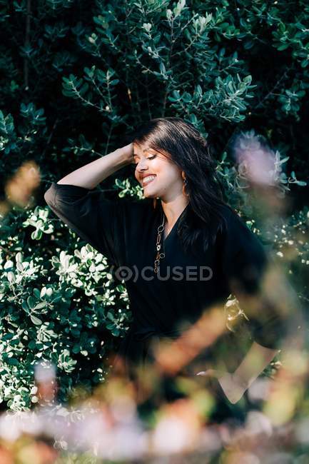 Beautiful brunette woman standing among blooming bushes in park and looking away in Lisbon — Stock Photo