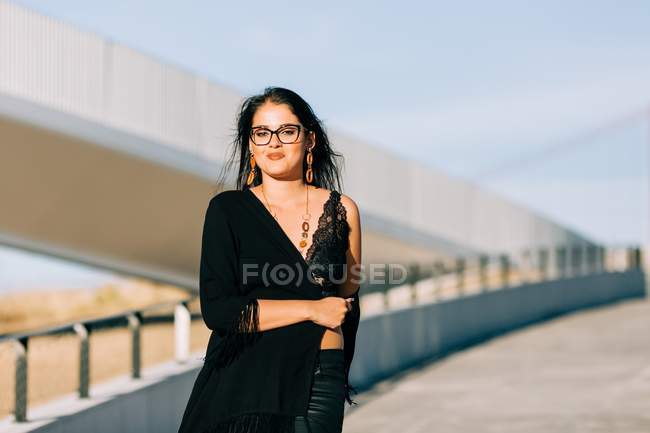 Beautiful stylish woman in black outfit standing by cable-stayed bridge in Lisbon on sunny day — стокове фото