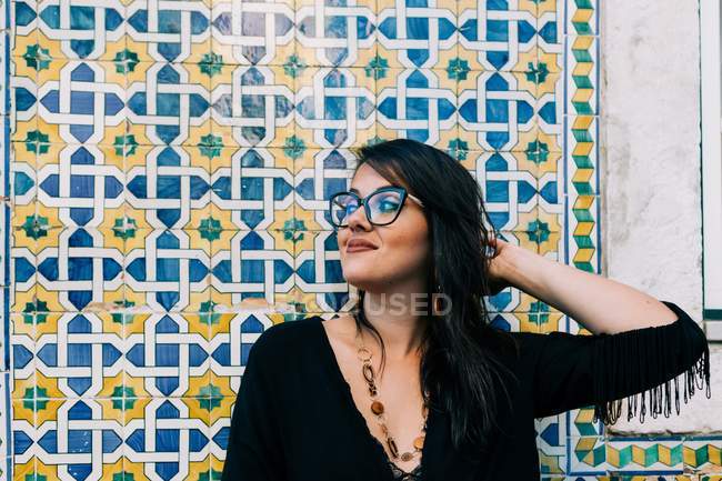 Приваблива молода жінка в окулярах і чорна блузка стоїть біля барвистого вінтажного муру і озирається в Лісабон — стокове фото