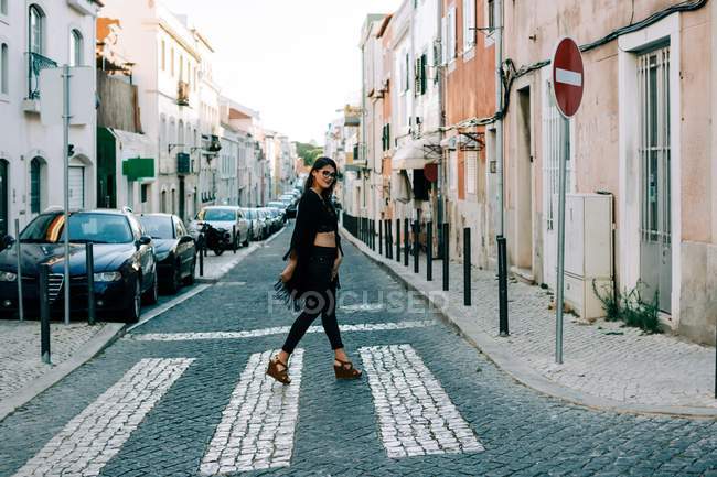 Модная молодая женщина в черном идет по пешеходной дорожке в Лиссабоне и улыбается — стоковое фото