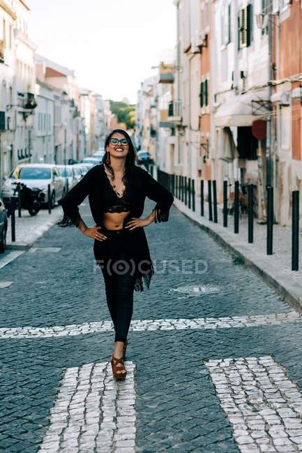 Дивна молода жінка в чорному одязі стоїть на перехресті з руками на стегнах у Лісабоні і посміхається — стокове фото