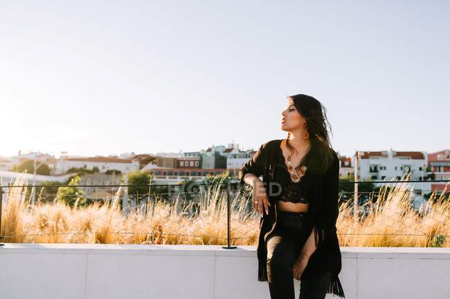Стильная женщина в черном наряде стоит у моста с городским пейзажем в Лисбоне в солнечный день — стоковое фото