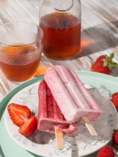 Refreshing strawberry popsicles on icy plate near glass of cold tea — Stock Photo