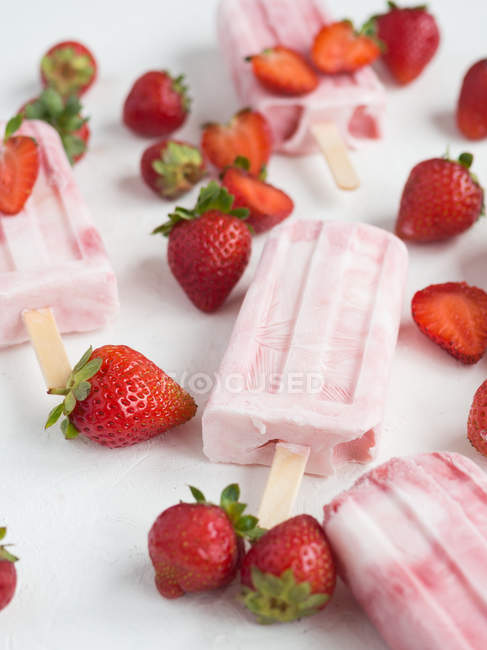 Primer plano de paletas rosadas y fresas frescas sobre fondo blanco - foto de stock