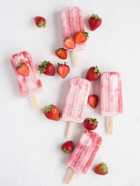 Von oben rosa Eis am Stiel und frische reife Erdbeeren auf weißem Hintergrund — Stockfoto