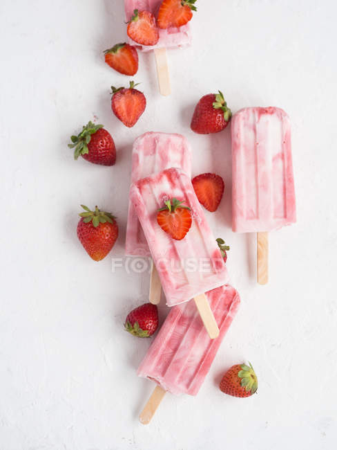 Von oben rosa Eis am Stiel und frische reife Erdbeeren auf weißem Hintergrund — Stockfoto