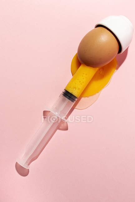 Яйцо для приготовления яиц в стакане со шприцем, вынимающим желток на розовом фоне — стоковое фото