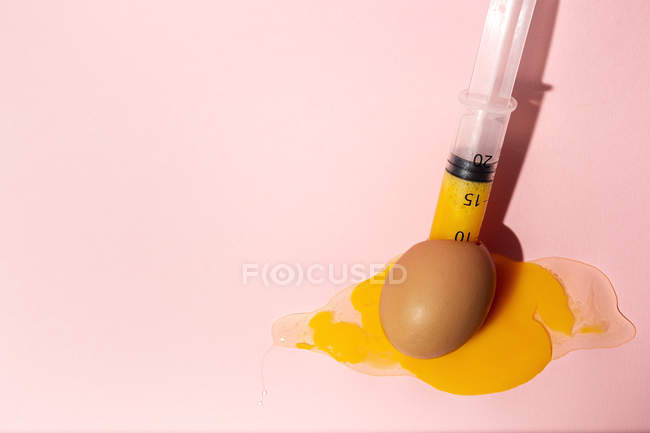 Kochei im Eierbecher mit Spritze, die gelbes rohes Eigelb auf rosa Hintergrund herausnimmt — Stockfoto