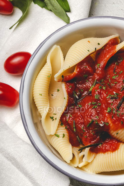 Delicious conchiglie pasta sprinkled with basil and red tomato sauce served on white plate — Stock Photo
