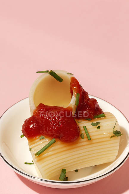 Приготовленные каннеллони с томатным соусом и травами подаются на белой тарелке на розовом фоне — стоковое фото