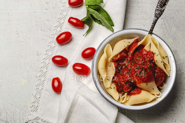 Delicious conchiglie pasta sprinkled with basil and red tomato sauce served on white plate — Stock Photo