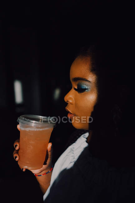 Retrato de vista lateral da bela jovem negra com maquiagem brilhante em vestido off-ombro tendo uma bebida gelada — Fotografia de Stock