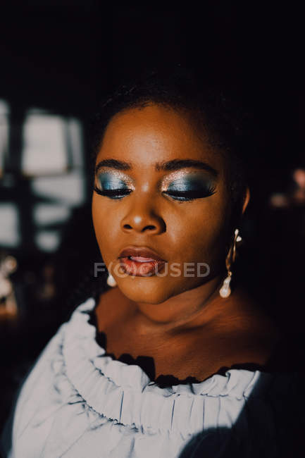 Портрет красивой пышной черной молодой женщины с ярким макияжем в платье без плеча, смотрящей вниз — стоковое фото
