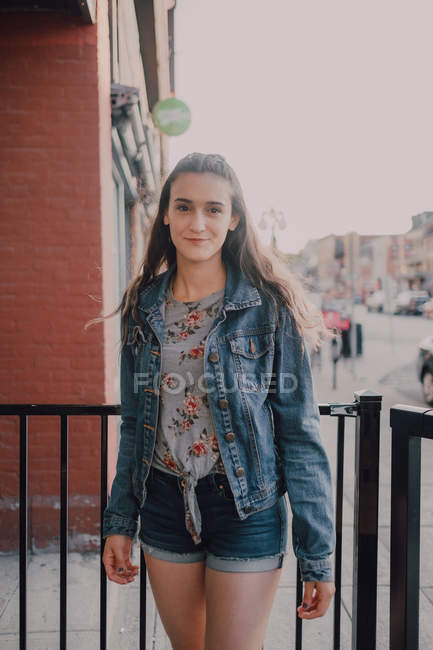 Woman with long hair in casual jeans jacket and shorts standing on street  on sunset, looking at camera — daylight, leisure - Stock Photo | #295764688
