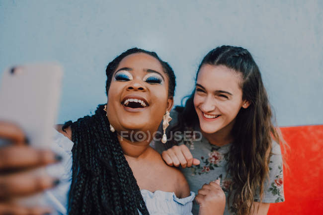 Multiracial young casual women laughing and taking selfie with smartphone on light background — Stock Photo