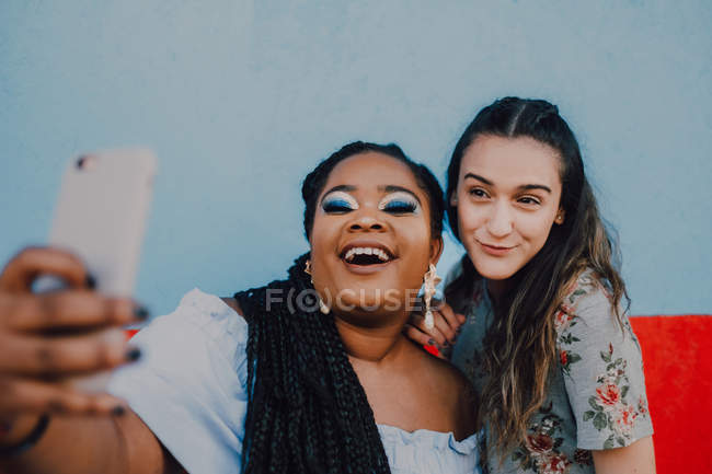 Mulheres casuais jovens multirraciais rindo e tirando selfie com smartphone no fundo claro — Fotografia de Stock