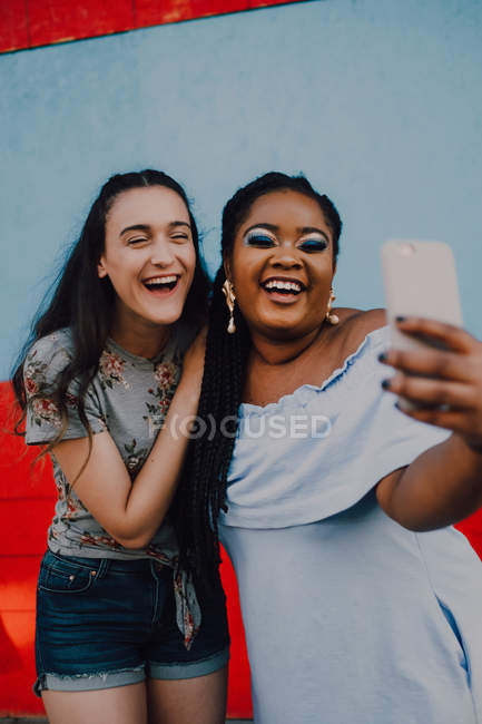 Multirazziale giovani donne casual ridere e scattare selfie con smartphone su sfondo chiaro — Foto stock