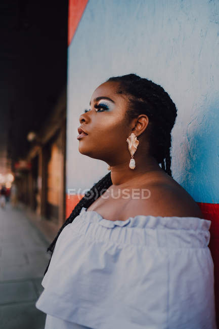 Attrayant moderne jeune femme noire jeune avec un maquillage lumineux en robe off-shoulder détournant les yeux — Photo de stock
