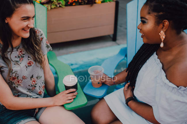 Fröhliche, multiethnische junge, lässige Frauen reden und trinken Kaffee, während sie am lebhaften Tisch im Hipster-Café sitzen — Stockfoto