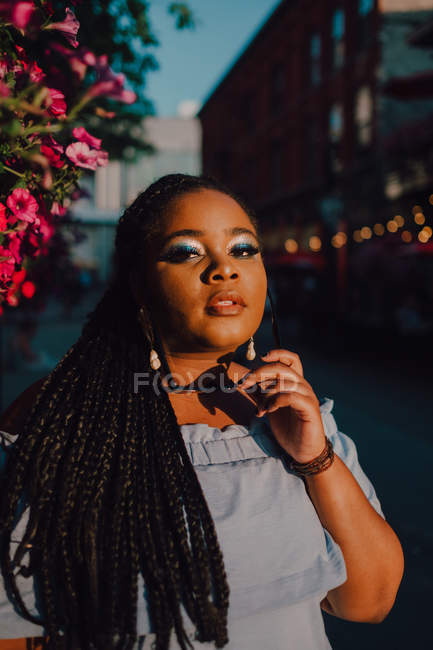 Attractive black stylish young woman in off-shoulder dress enjoying sunshine while standing on street — Stock Photo