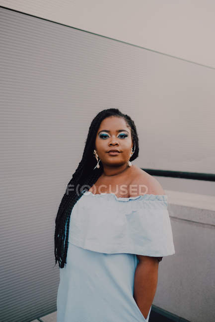 Attraktive schwarze junge Frau mit hellem Make-up im Off-Shoulder-Kleid steht auf einer leeren Wand und blickt in die Kamera — Stockfoto