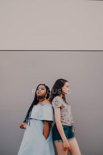 Молодые женщины разных рас смеются и обнимаются, стоя на стене улицы. — стоковое фото