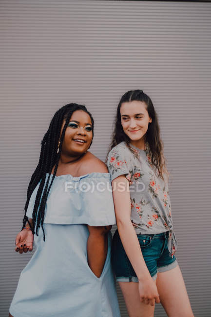Multiracial young casual women laughing and hugging while standing on street wall — Stock Photo