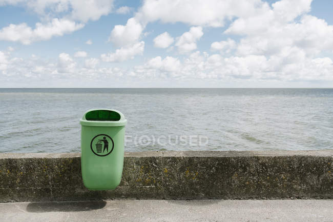 Grüner Mülleimer auf sauberem, leerem Betonstreifen am Strand an bewölkten Tagen — Stockfoto