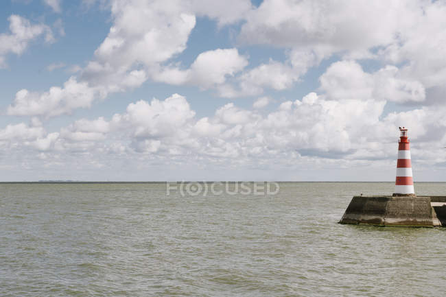 Полосатый маяк на берегу моря в облачный день — стоковое фото