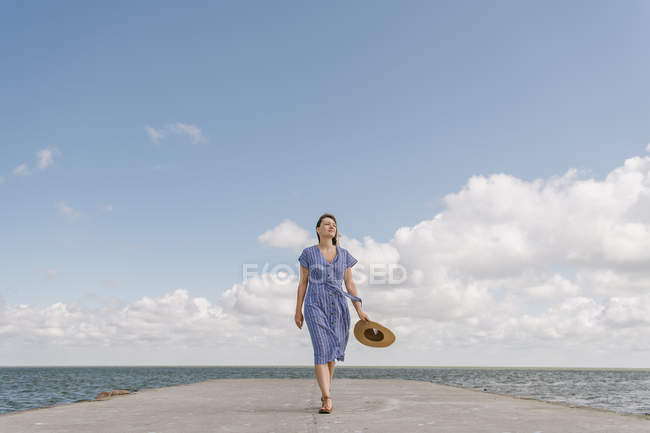 Back view of adult woman in straw hat and sundress on empty concrete quay on cloudy day — Stock Photo