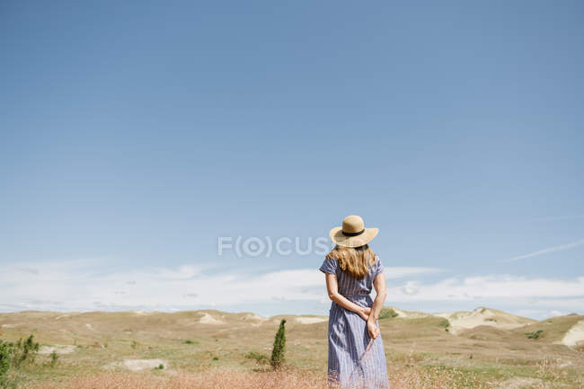 Back view of adult woman in dress with wisp of dry grass spikes while standing on scenic field, Nida — Stock Photo