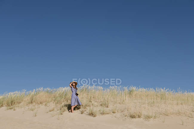 Rückansicht einer erwachsenen Frau mit Strohhut und Kleid mit Kamera auf einem Hügel stehend — Stockfoto