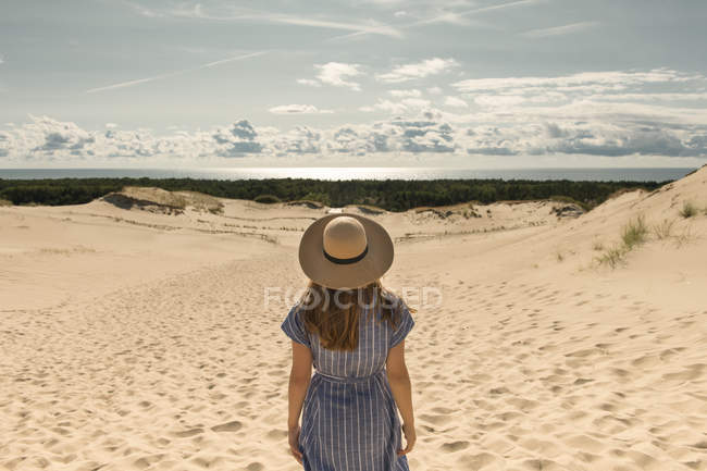 Adult woman in casual dress and straw hat standing on sand dune on hot summer day — Stock Photo