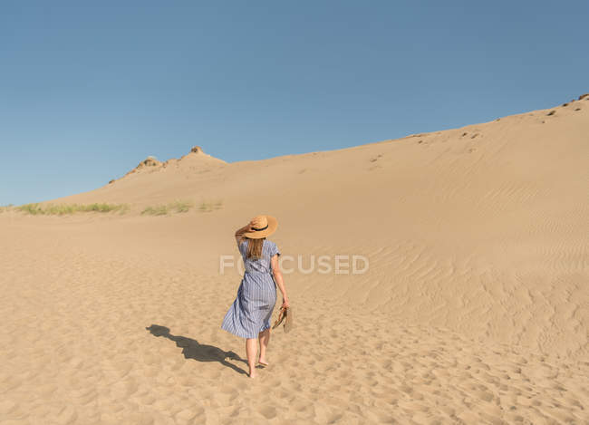 Доросла жінка в повсякденному одязі і солом'яному капелюсі, що добре проводить час на піщаній дюні в спекотний літній день — стокове фото