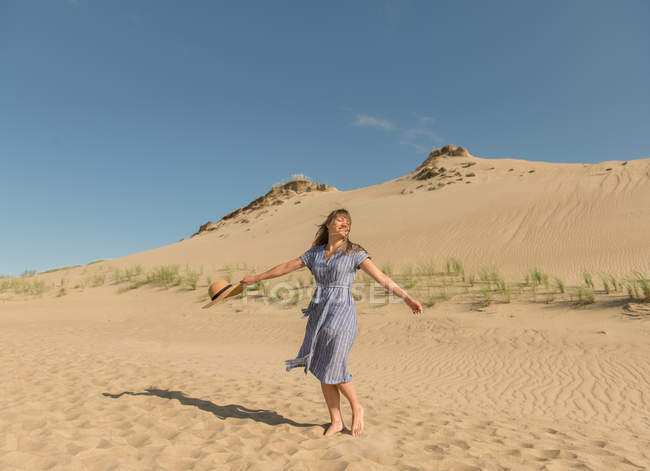 Adult woman in casual dress and straw hat running having good time on sand dune on hot summer day — Stock Photo