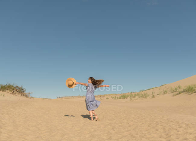 Доросла жінка в повсякденному одязі і солом'яному капелюсі добре проводить час на піщаній дюні в спекотний літній день — стокове фото