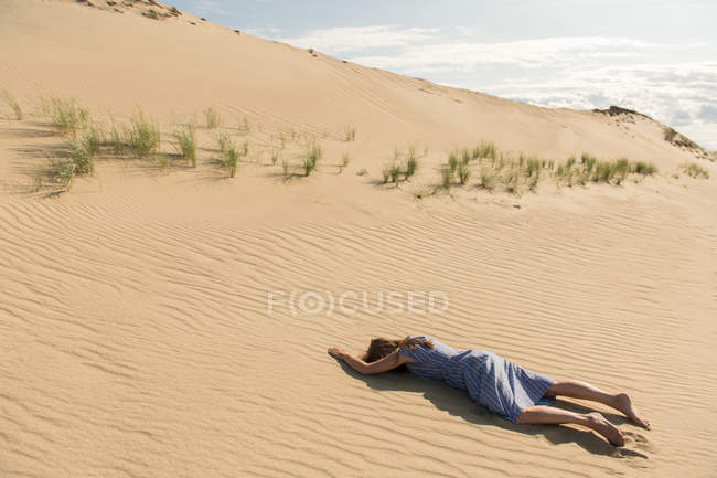 Mujer en vestido casual acostada con la cara hacia abajo en la duna de arena en el día de verano caliente - foto de stock