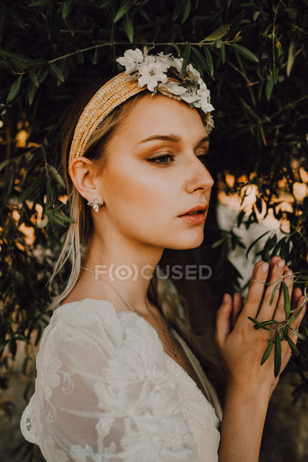 Affascinante donna in abito elegante con fiori vicino albero — Foto stock