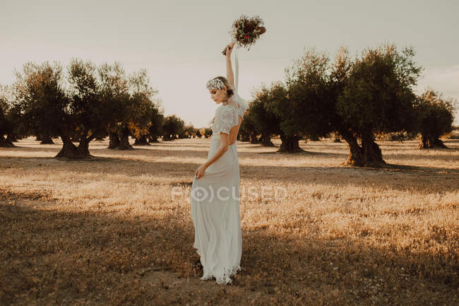 Content woman in dress with open back raising hands with flower bouquet — Stock Photo