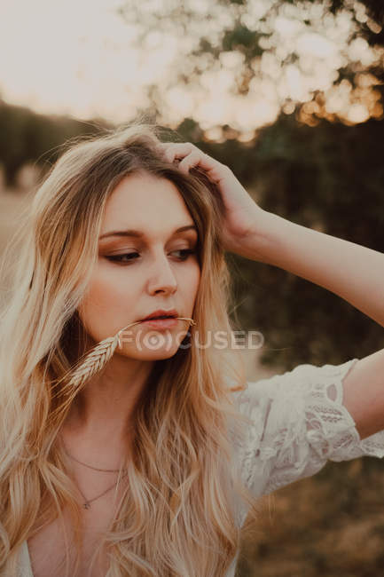 Mujer hermosa reflexiva con el pelo que fluye y paja en la boca - foto de stock