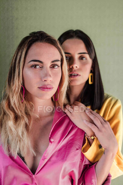 Attractive stylish gorgeous calm females in vibrant fashionable outfit looking at camera confidently while touching hands — Stock Photo